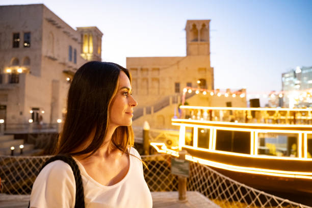 Side view portrait of female tourist on Al Fahidi waterfront with illuminated boat