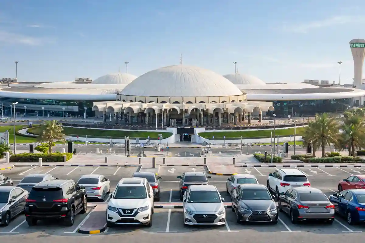 Sharjah International Airport terminal with cars parked in the parking area in front